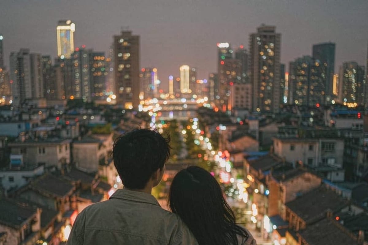 Casal em terraço olhando a cidade chinesa à noite, de costas
